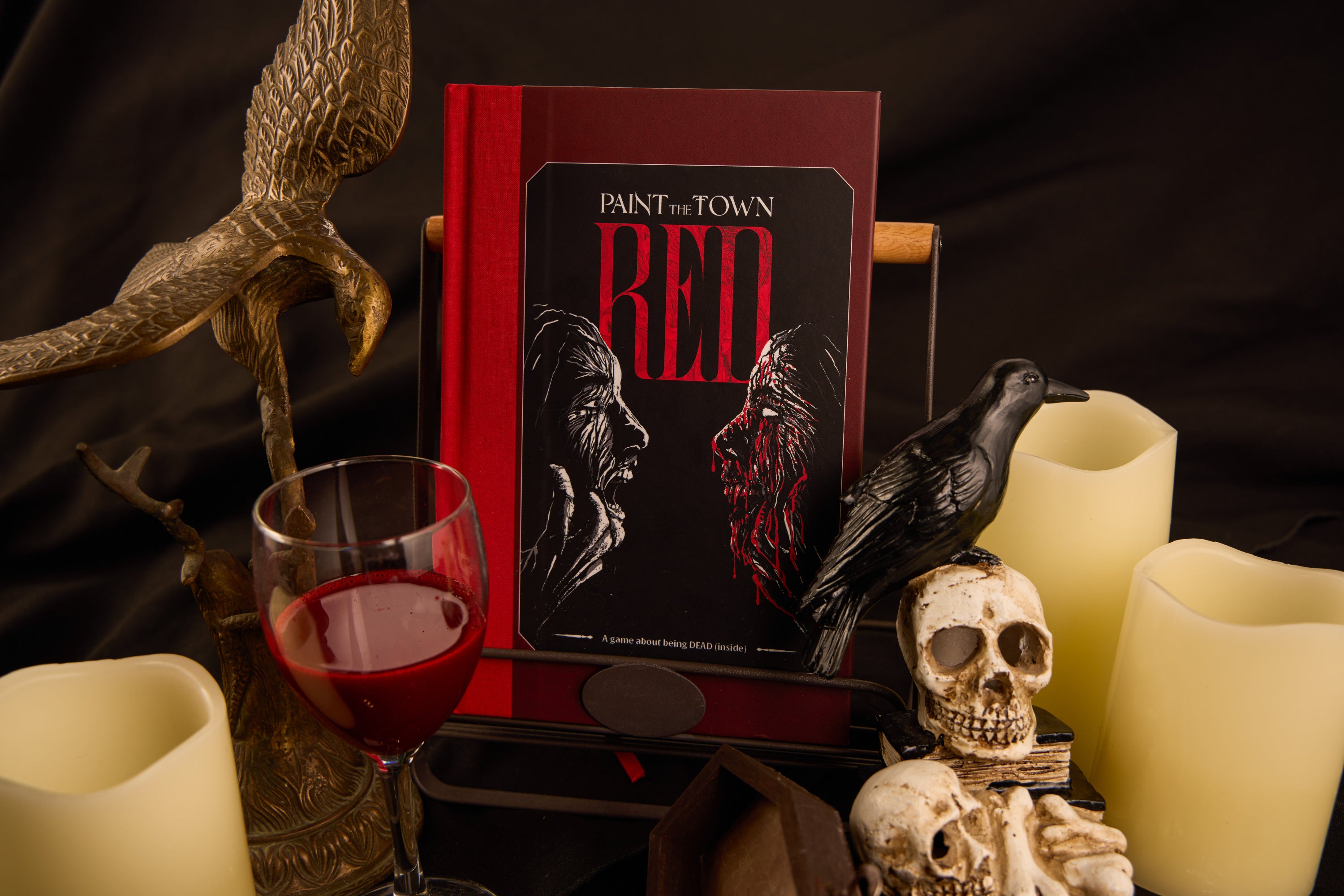 Book titled 'Paint the Town Red' with a glass of red wine, candles, and decorative items on a dark background.